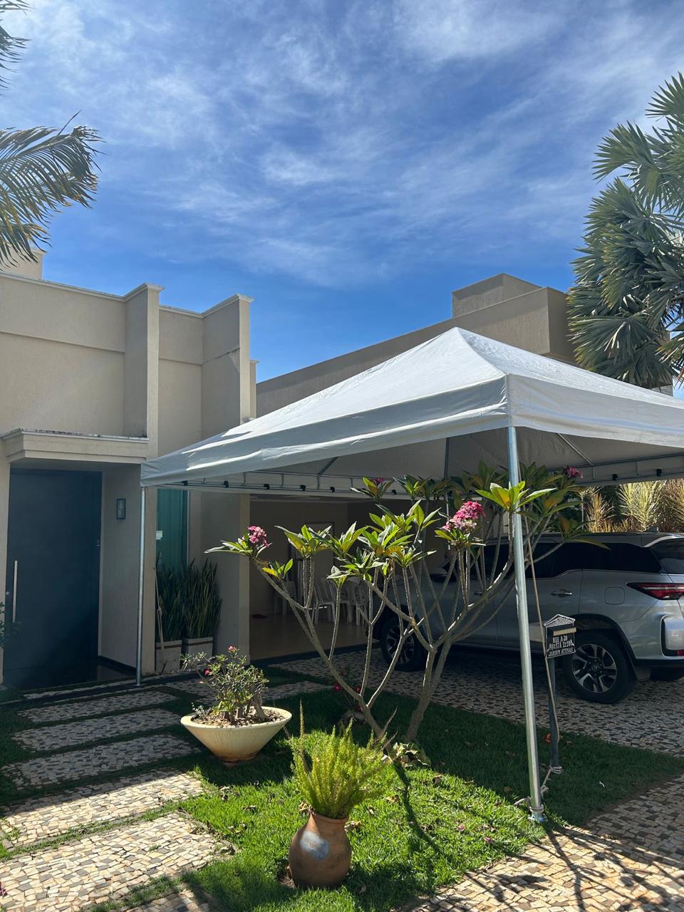 Tenda piramidal branca montada na entrada de uma casa, cobrindo a área da garagem
